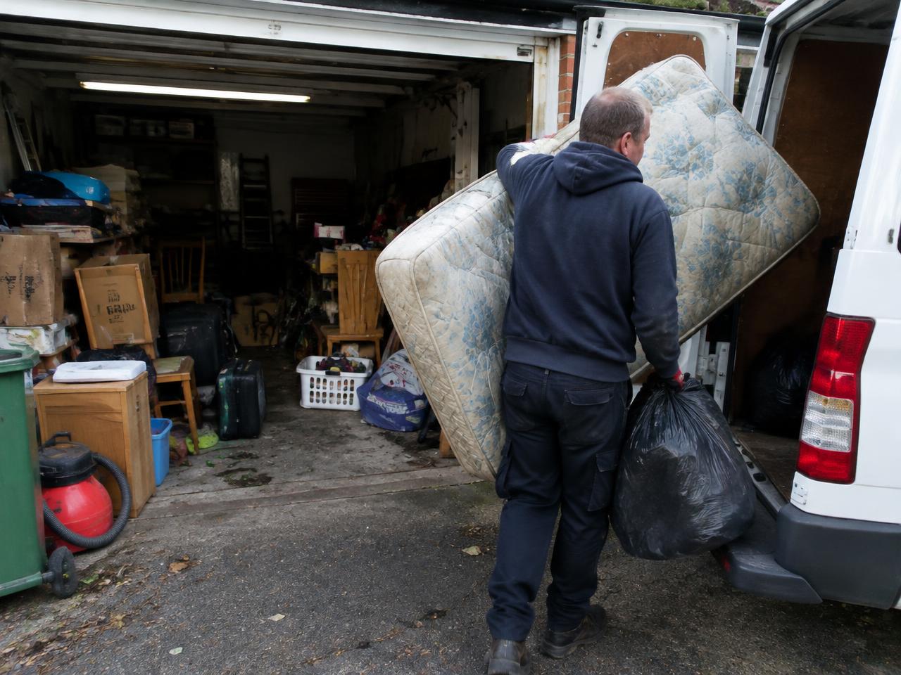 Worker removing an old mattress and rubbish from a garage into a van